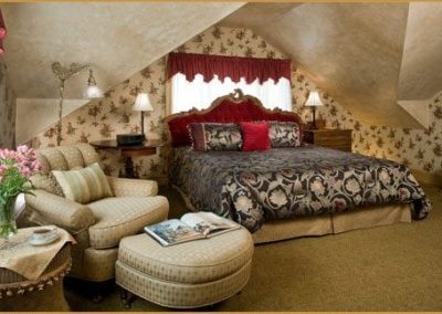 Photo of the Crown Jewel bedroom featuring a king bed with a dramatic red velvet headboard and cozy chair with ottoman