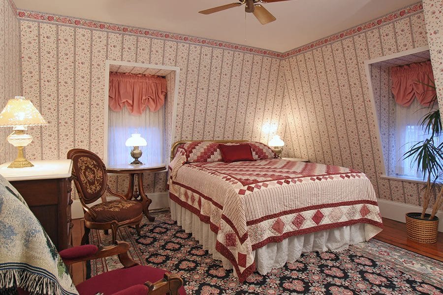 Buckingham guestroom Queen Bed with burgundy patterned quilt with black and rose floral area rug.