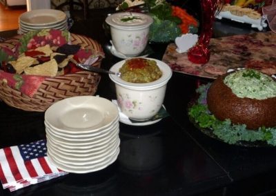 Prince Albert Hall dining room table set with American flag napkins for a Memorial Day celebration. Spinach dip in a rye bread bowl, guacamole spread and a basket of tortilla chips. are also on the table.