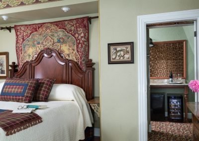 Close up of Crown Prince Guestroom's Elegant Solid Wood King headboard with beautiful tapestry behind it. Also a closeup of the hall into the guestroom's private sitting room with wetbar.