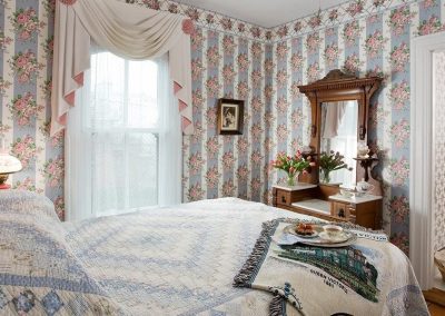 Lillie Langtry guestroom bedroom with queen bed and antique mirrored dresser. Pink and blue floral wallpaper.
