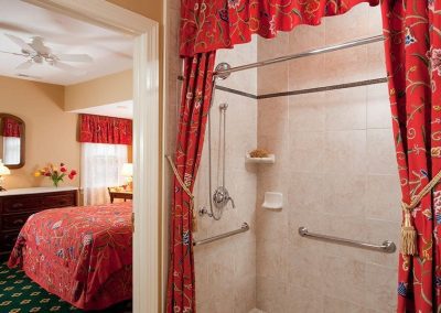 Regents Park tiled shower with handrails and vibrant red floral draperies surrounding it.
