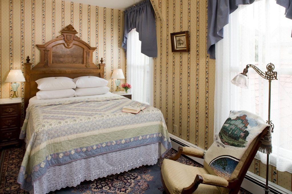 The Charles Dickens guestroom bedroom with a queen bed with a beautiful blue and purple quilt. The solid wood antique headboard is stately.
