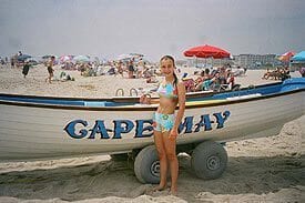 Guest Photos- Girl standing next to small boat at beach.
