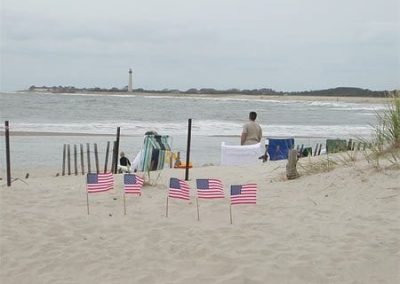 Small American flags on beach with people near ocean.